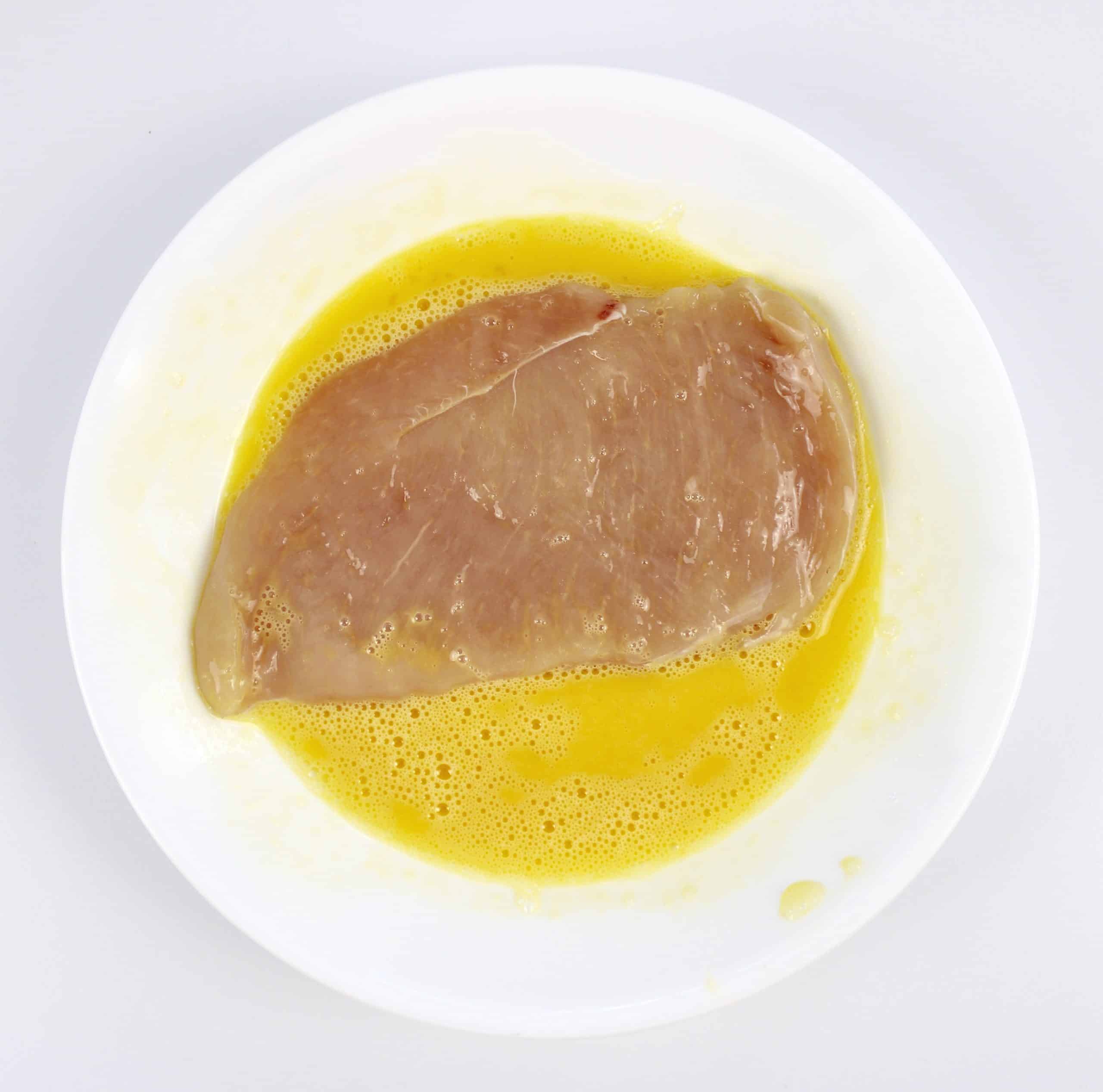 chicken breast in white bowl with beaten egg