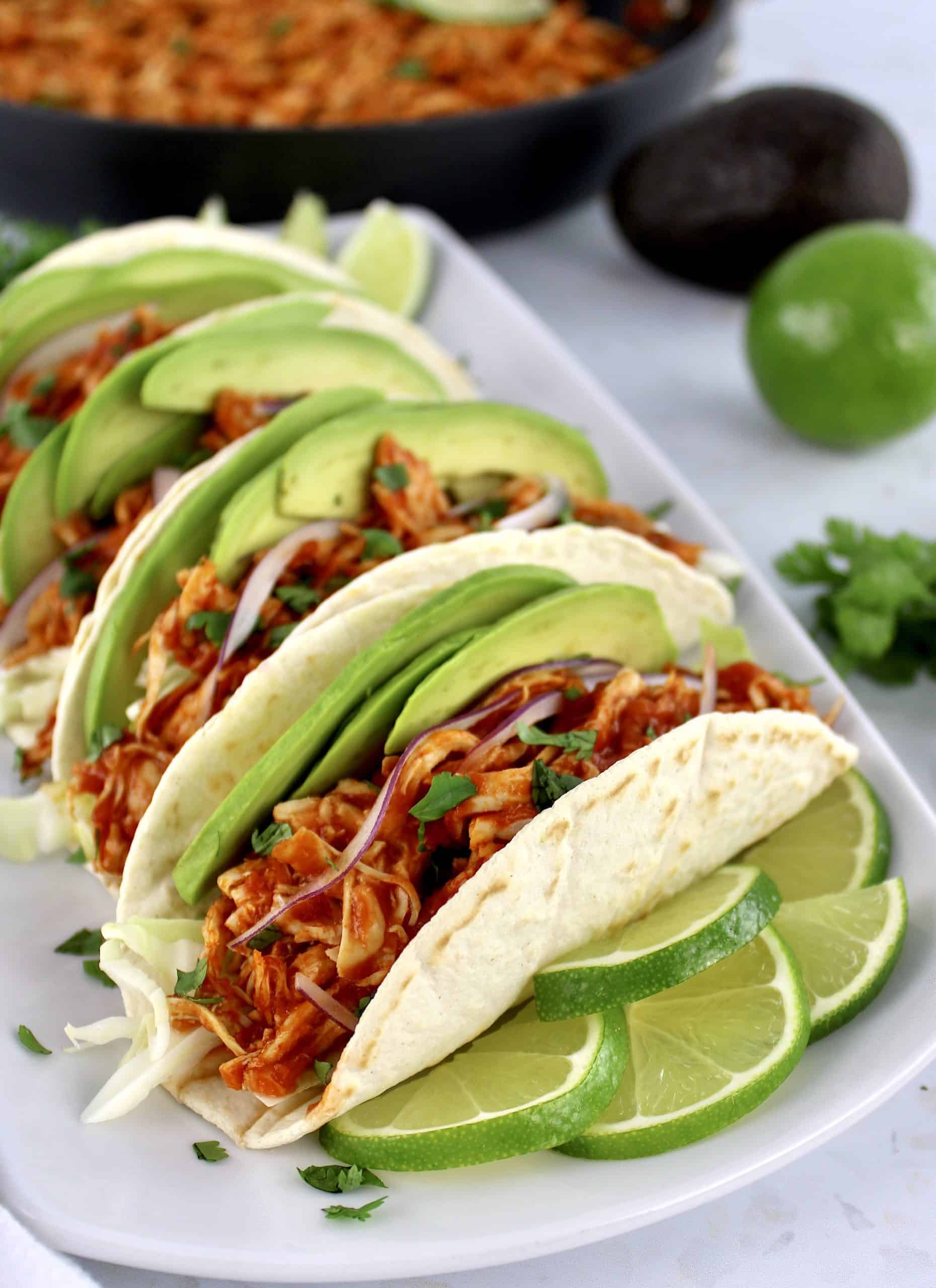 closeup of Chicken Tinga in tortillas on white plate with limes slices on side