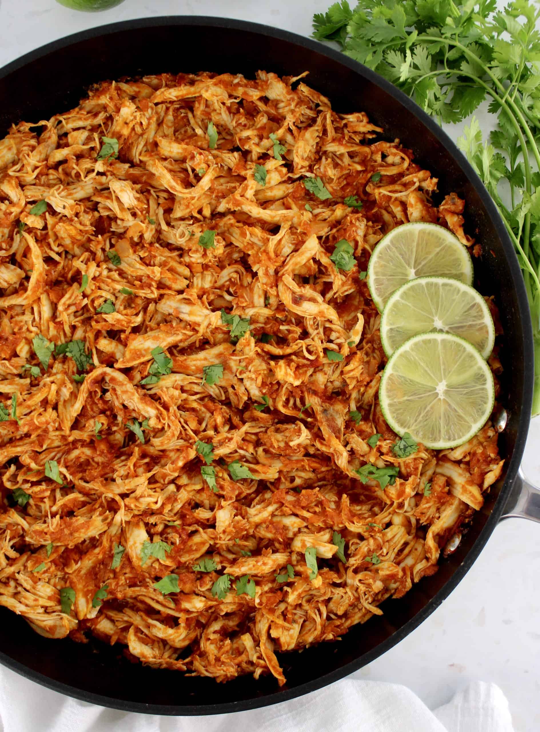 Chicken Tinga in skillet with 3 slices of lime on side