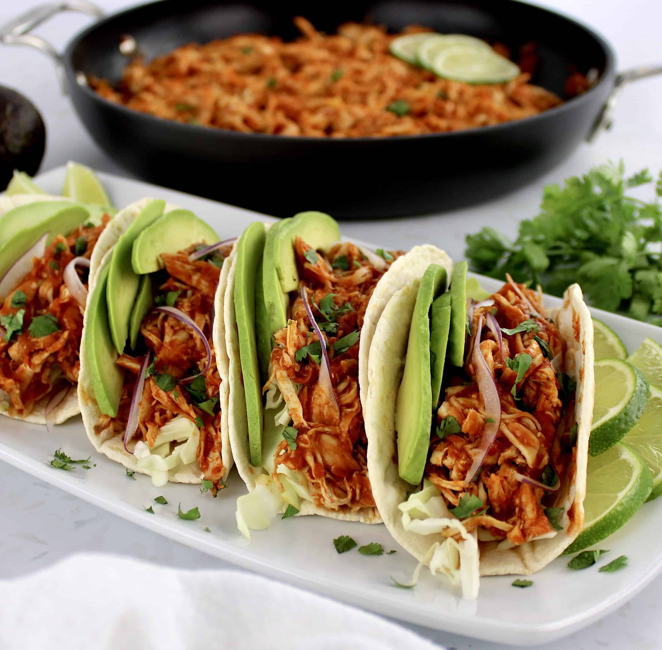 closeup of Chicken Tinga in tortillas on white plate with limes slices on side
