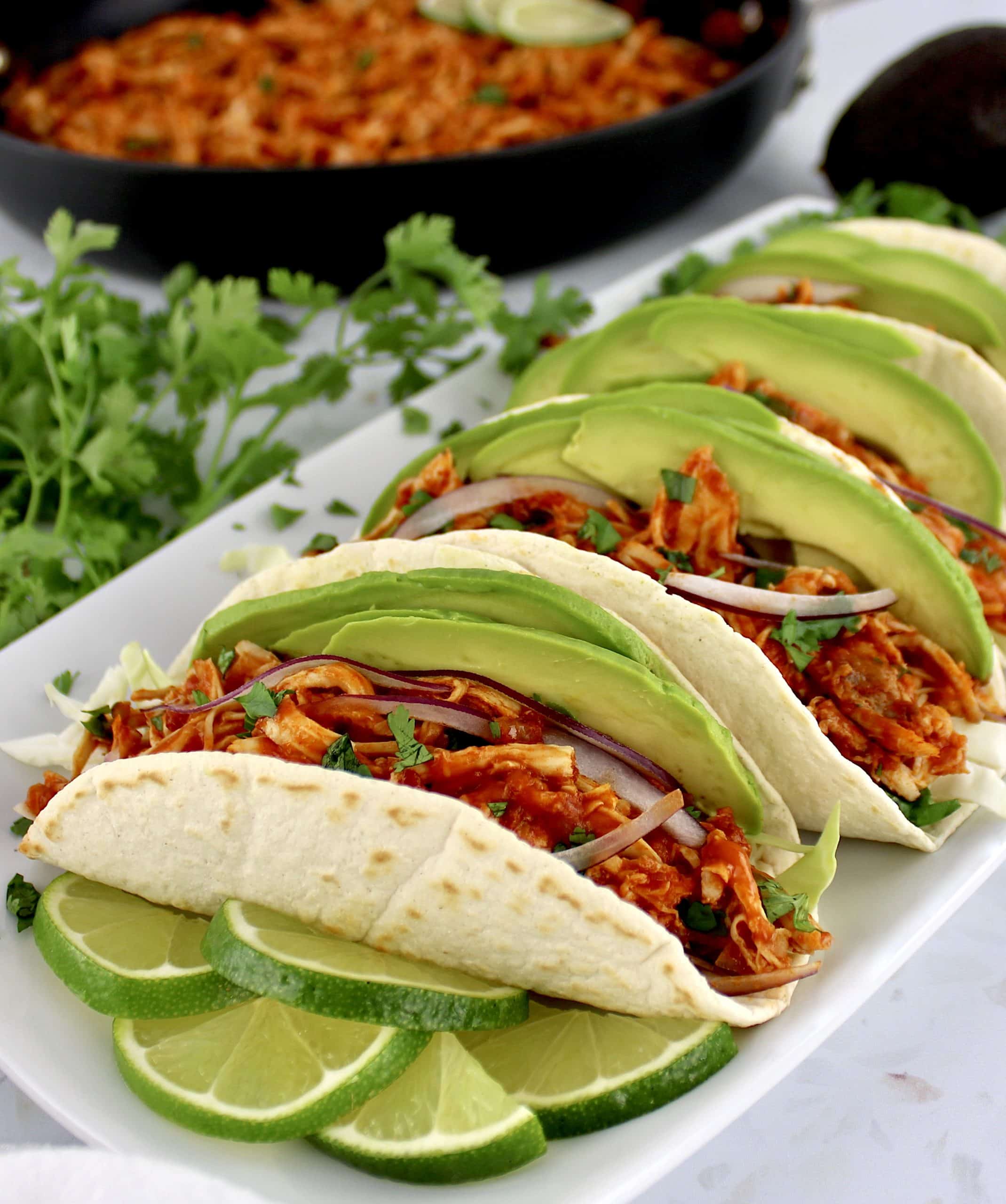 closeup of Chicken Tinga in tortillas on white plate with limes slices on side