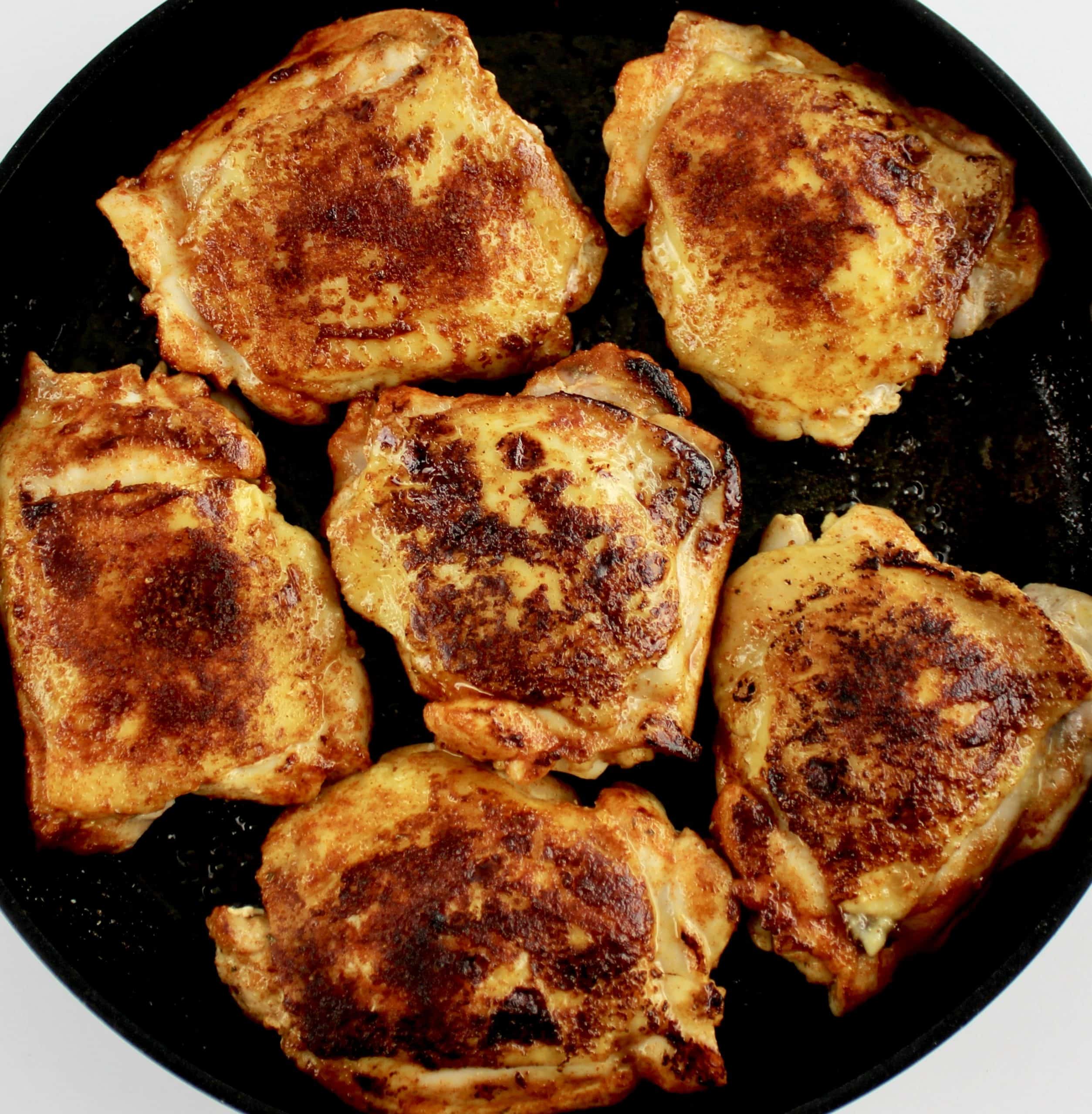 6 seared chicken thighs in skillet with paprika seasoning