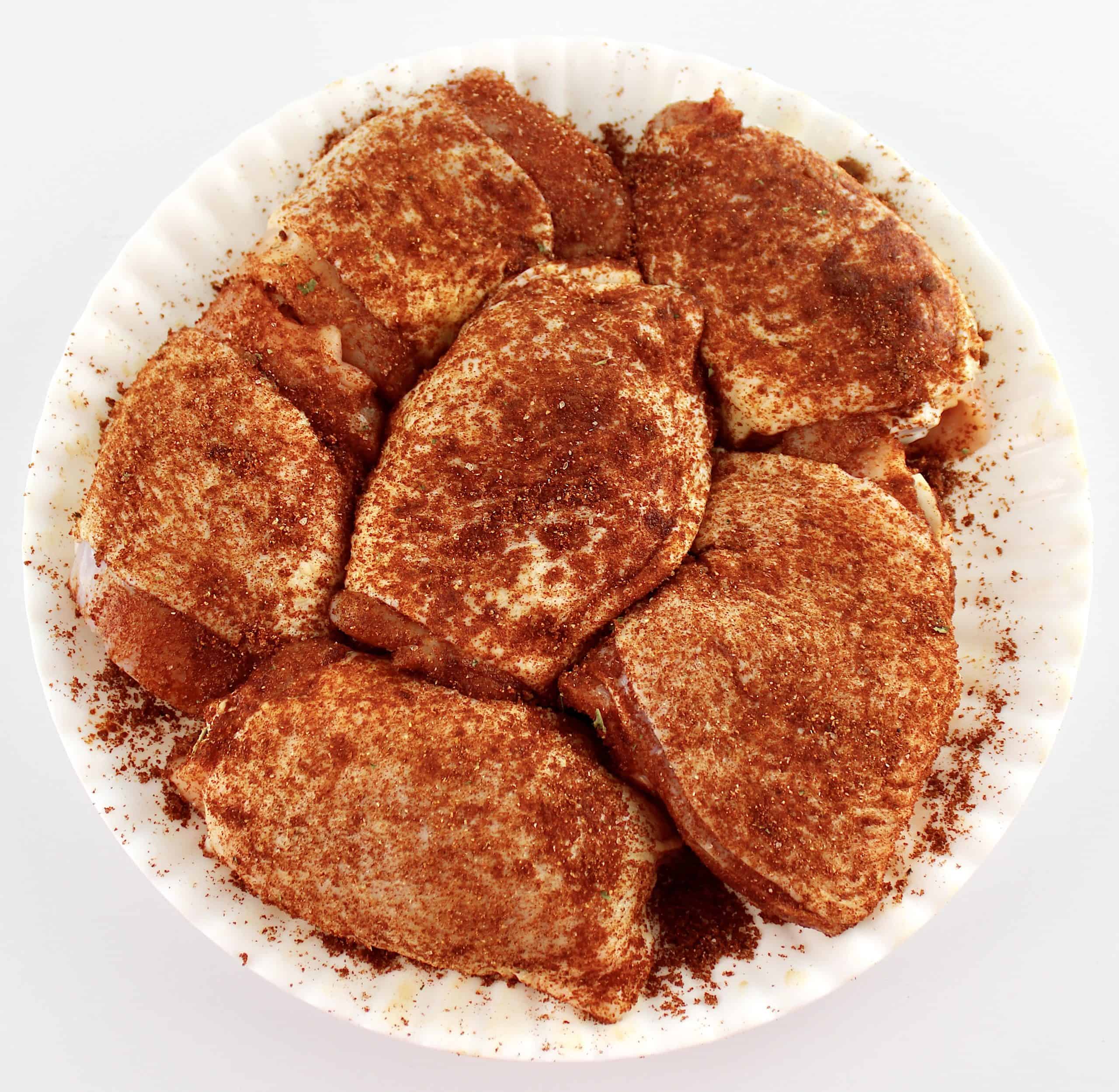 6 chicken thighs on white plate with paprika seasoning all over
