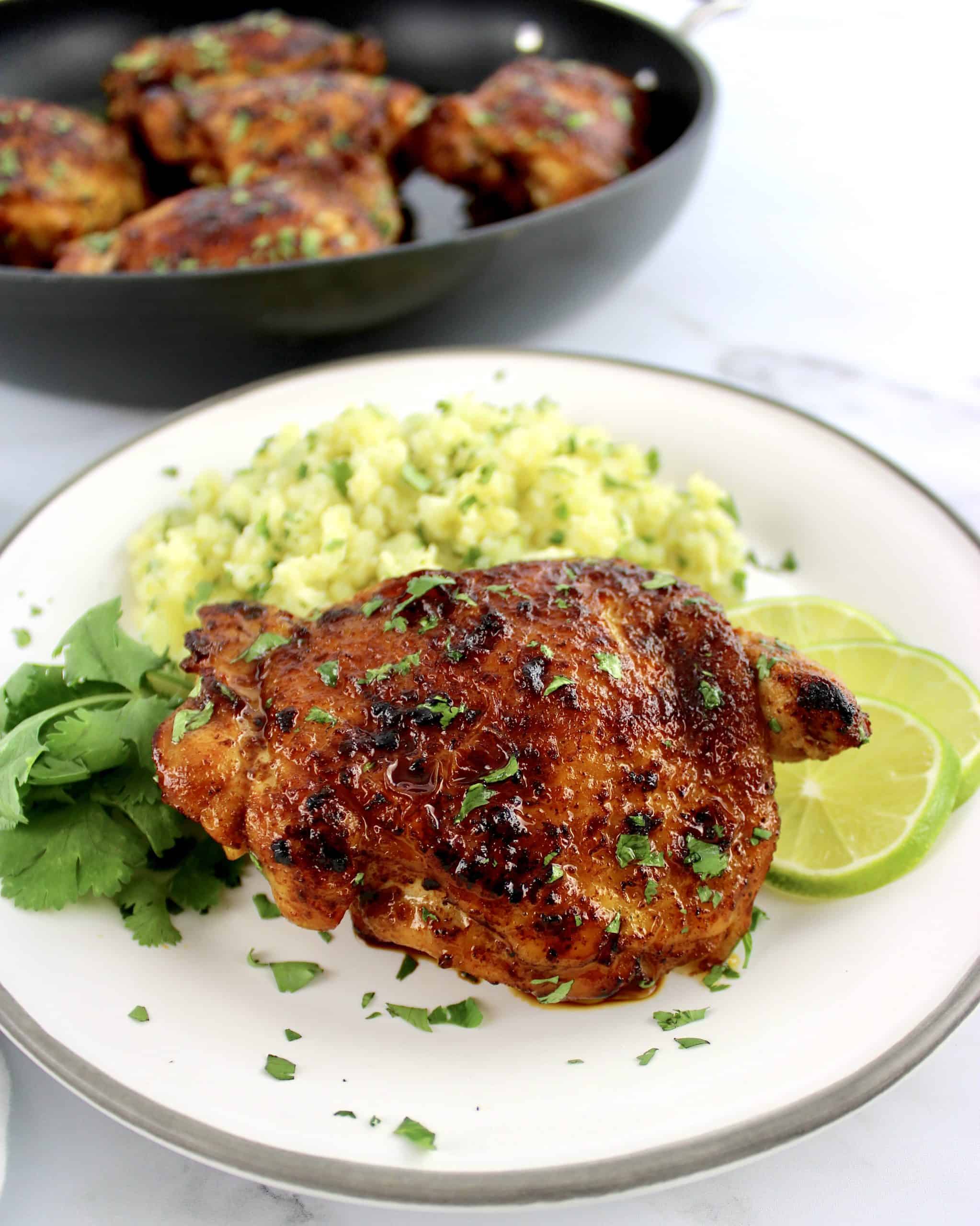 Paprika Chicken Thigh on white plate with cilantro cauliflower rice cilantro and lime slices on side