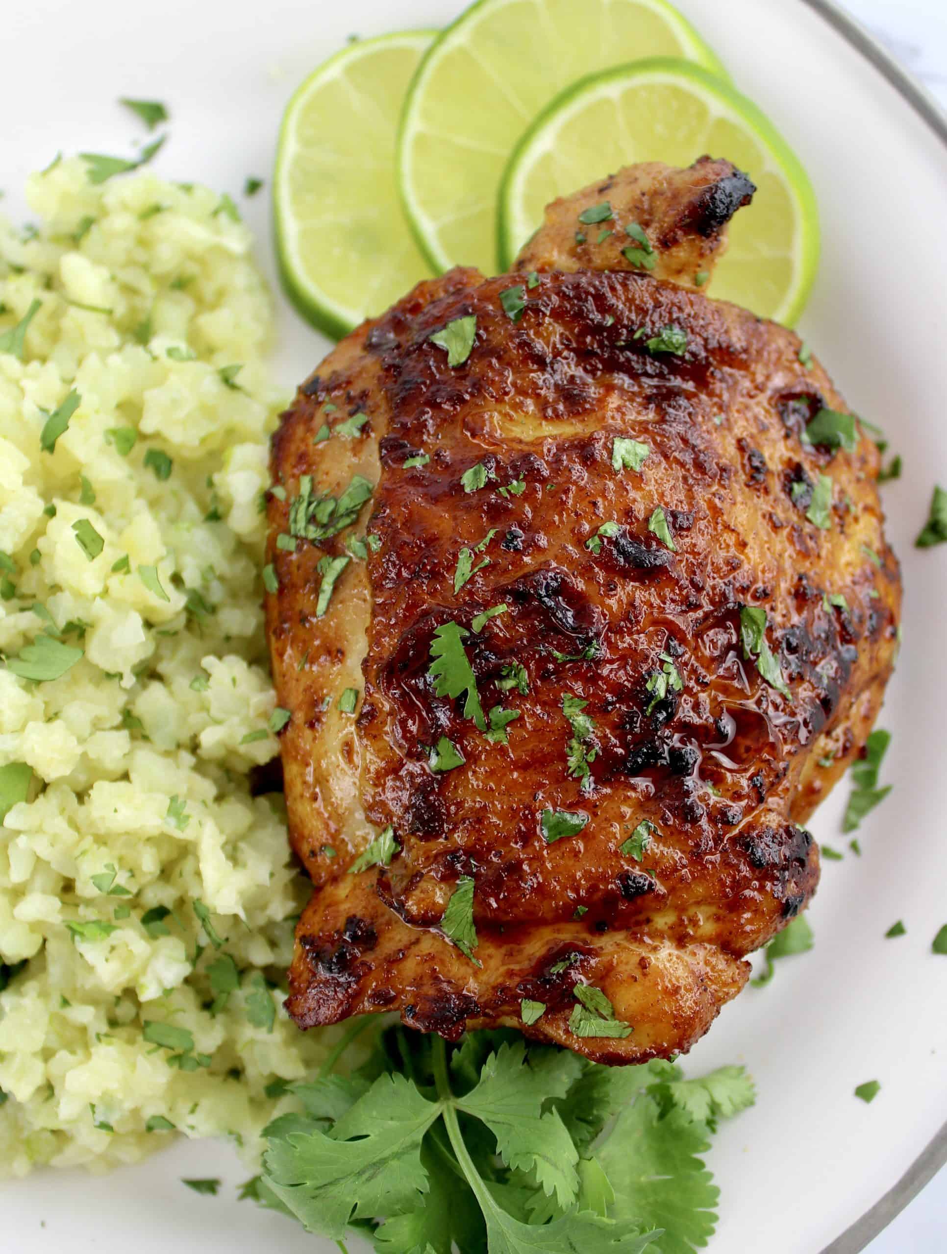 Paprika Chicken Thigh on white plate with cilantro cauliflower rice cilantro and lime slices on side