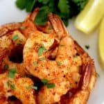 Air Fryer Frozen Shrimp stacked up on white plate with lemon wedge and parsley on side