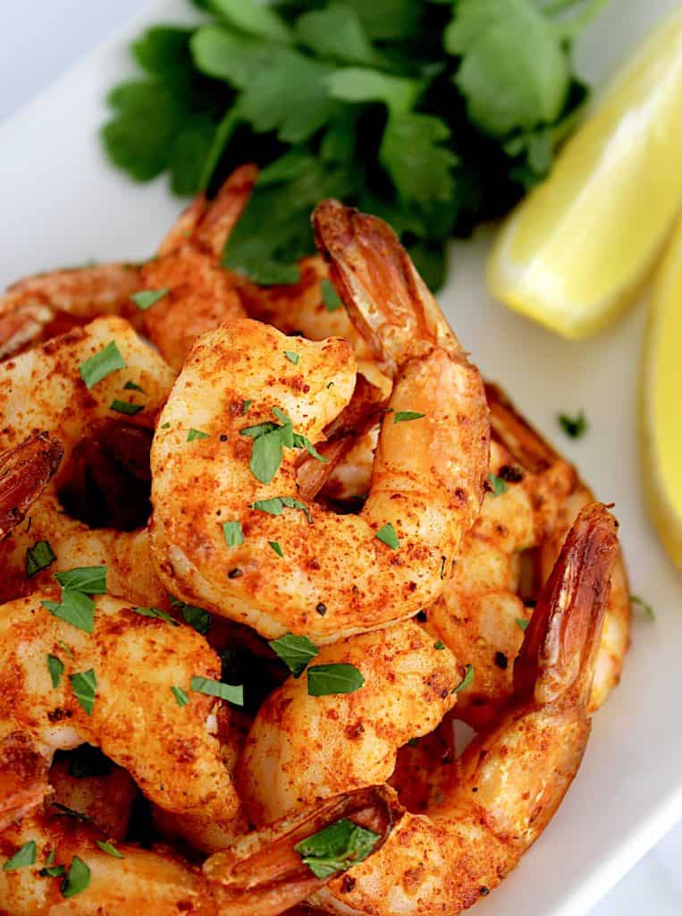 Air Fryer Frozen Shrimp stacked up on white plate with lemon wedge and parsley on side