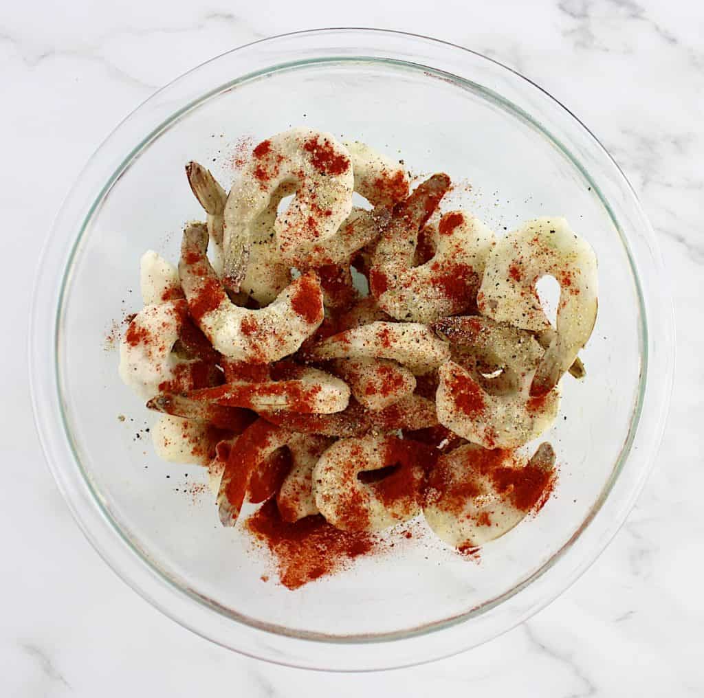 raw frozen shrimp in glass bowl with spices on top