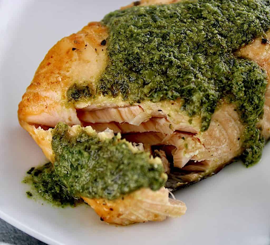 closeup of cut open salmon with pesto on top