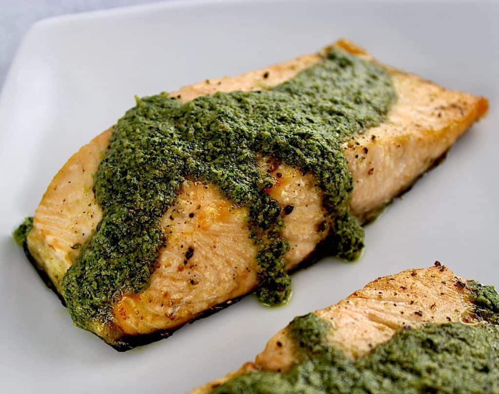 closeup of piece of Air Fryer Pesto Salmon on plate with pesto sauce on top and dripping down the sides