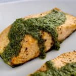 closeup of piece of Air Fryer Pesto Salmon on plate with pesto sauce on top and dripping down the sides