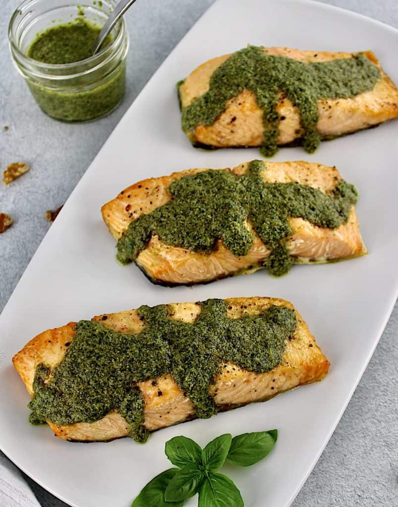 overhead view of 3 pieces of Air Fryer Pesto Salmon on white plate with pesto sauce in open jar in background