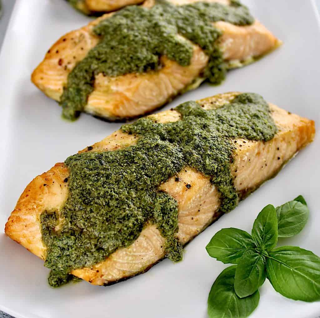 closeup of piece of Air Fryer Pesto Salmon on plate with pesto sauce on top and dripping down the sides