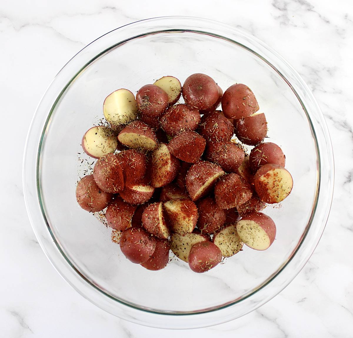 cut red potatoes in glass bowl with olive oil and spices on top