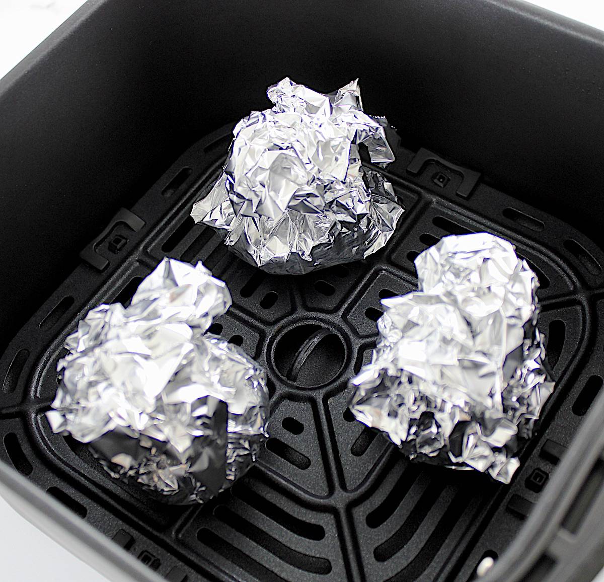 3 bundles of garlic wrapped in foil in air fryer basket