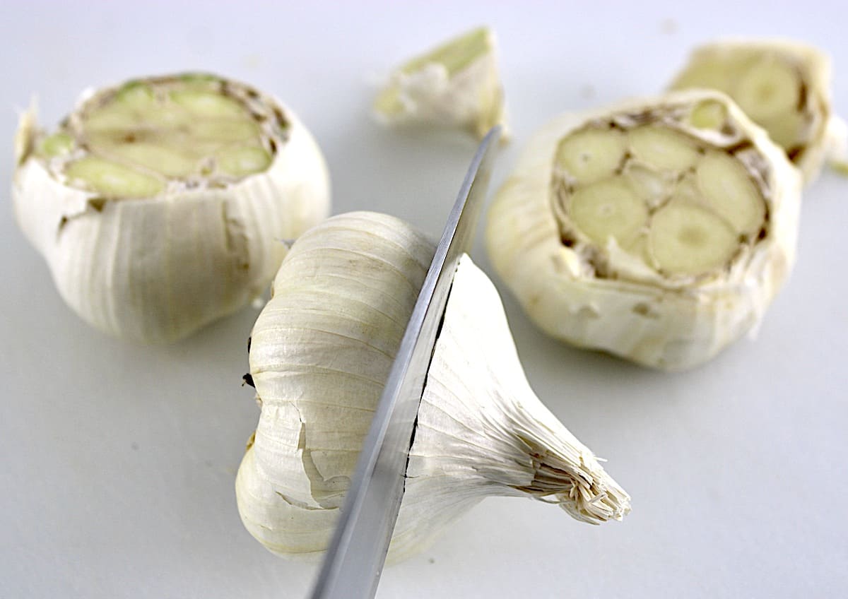 head of garlic being cut with knife with cut garlic heads in background