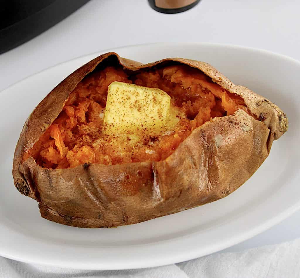 closeup of sweet potato on white oval plate with butter and cinnamon