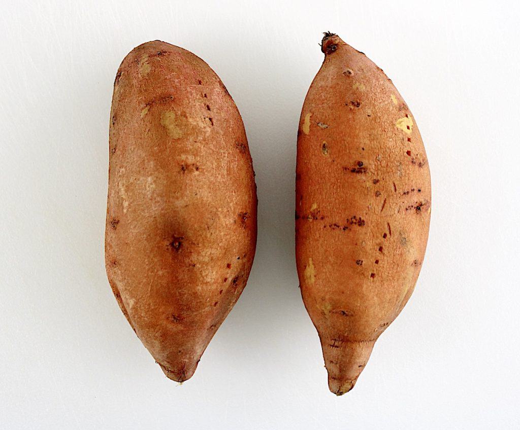 2 raw sweet potatoes with with holes poked in them on white cutting board