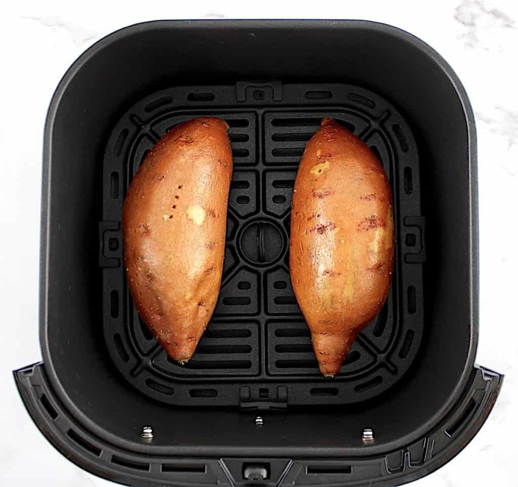 2 raw sweet potatoes in air fryer basket with olive oil and salt