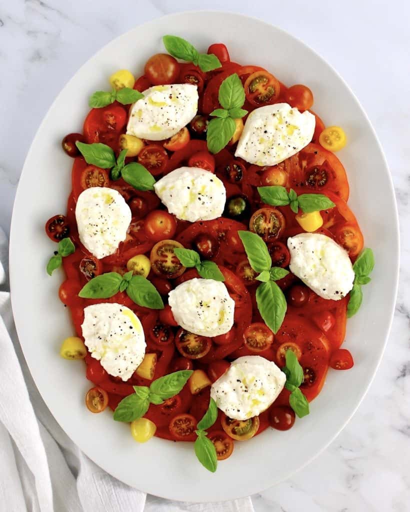 Burrata Caprese on white oval platter with basil leaves around