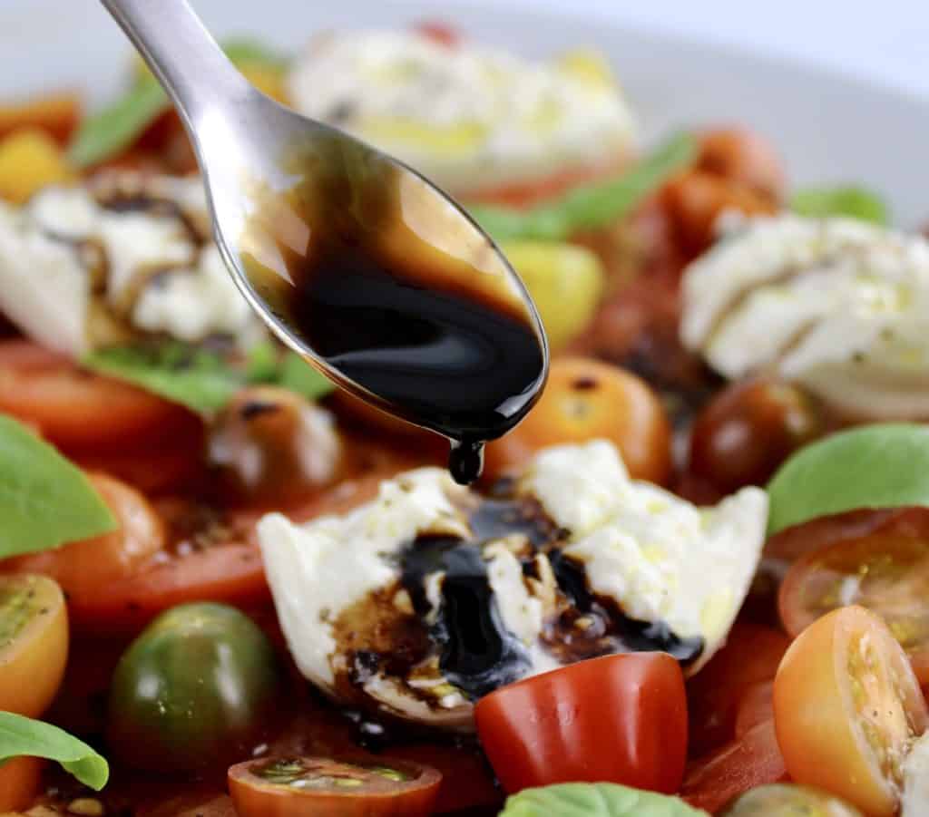 Burrata Caprese with balsamic reduction being spooned over top of cheese