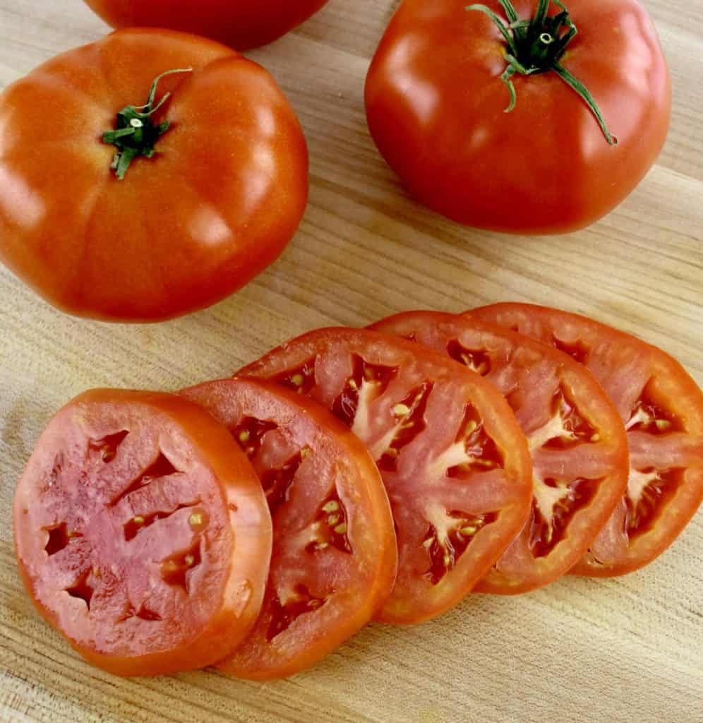 vine ripe tomato sliced on cutting board with tomatoes in background