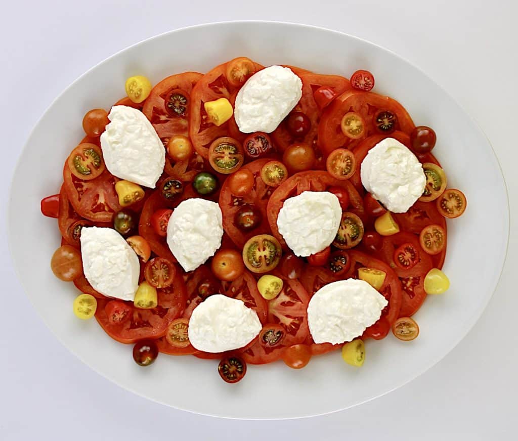 Burrata Caprese salad on white oval platter without dressing