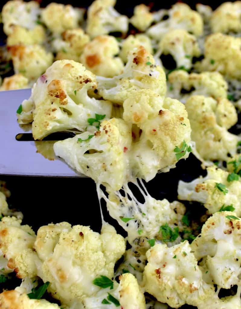 Cheesy Roasted Cauliflower being lifted off sheet pan with silver spatula