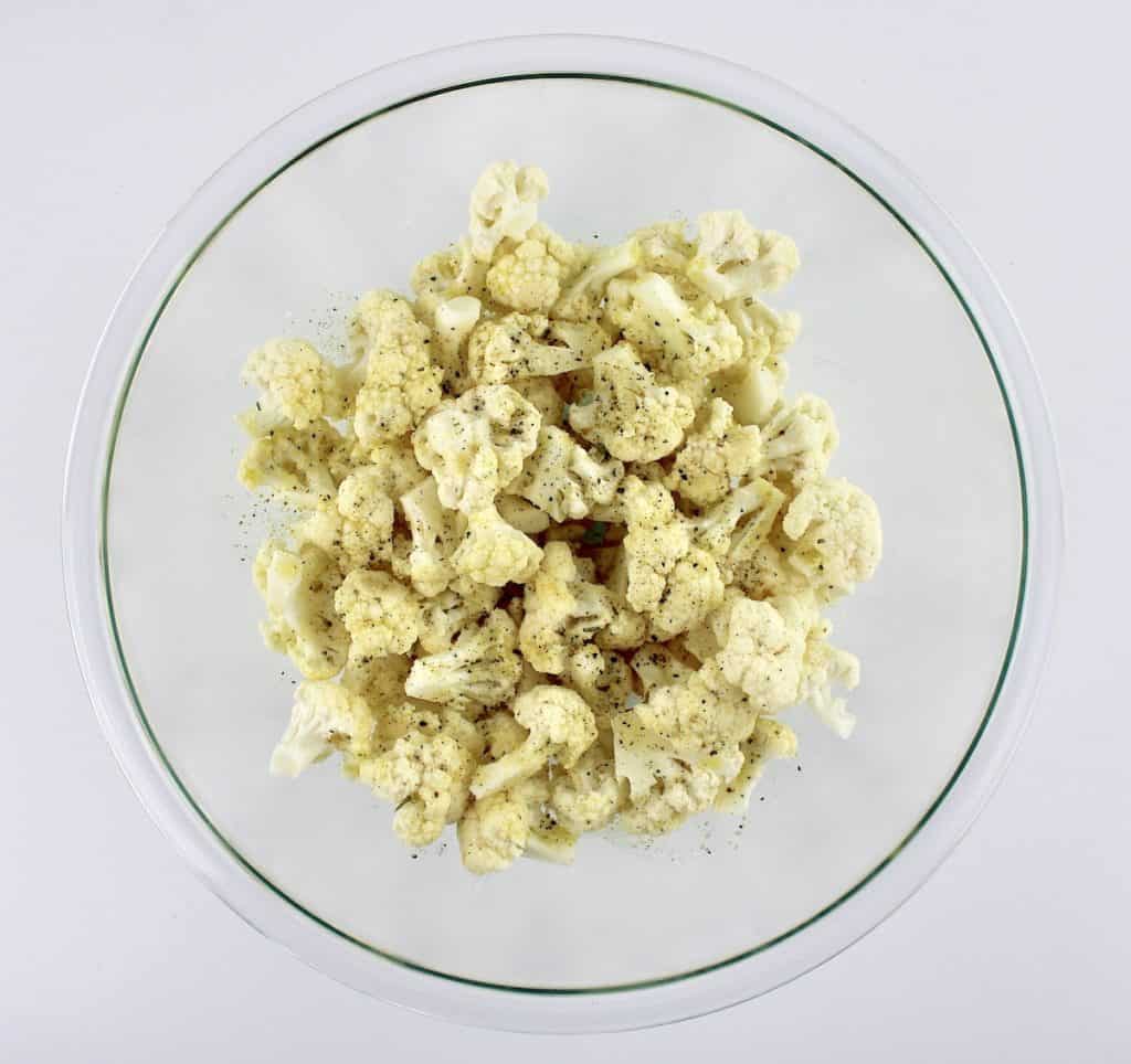 cauliflower florets in glass bowl with garlic salt and olive oil on top