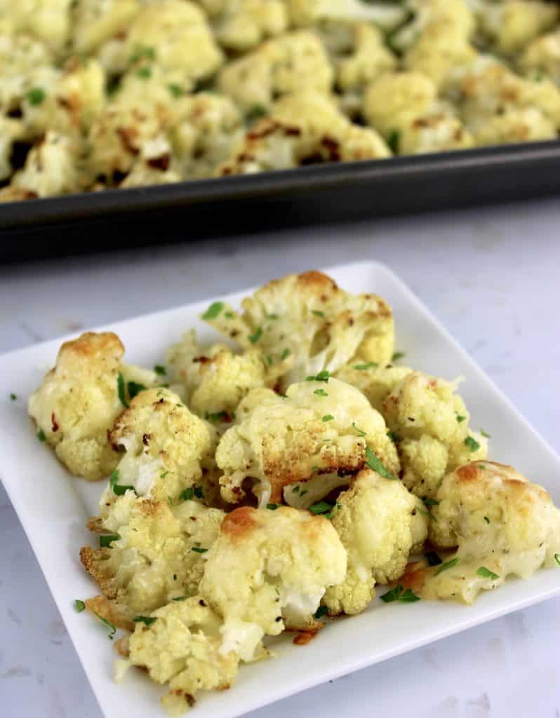 Cheesy Roasted Cauliflower on white square dish with baking sheet in background