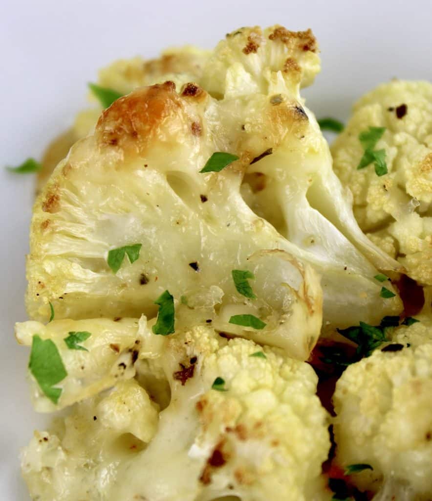 closeup of Cheesy Roasted Cauliflower on white plate with chopped parsley on top