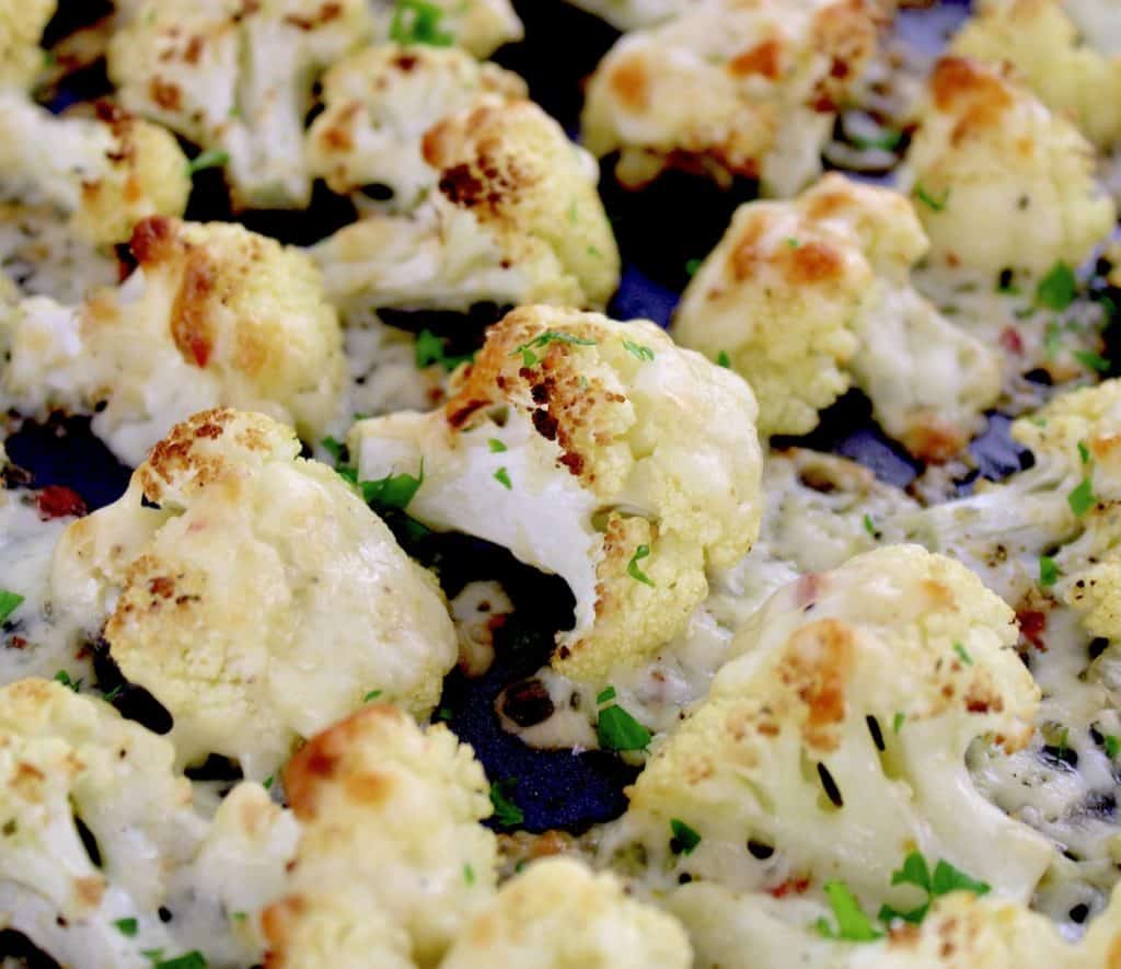 closeup of Cheesy Roasted Cauliflower on baking sheet with chopped parsley garnish