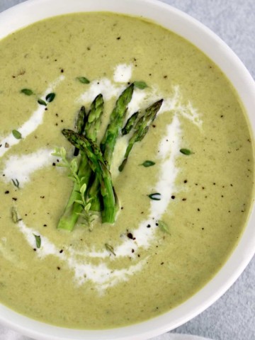 Cream of Asparagus Soup in white bowl with splash of heavy cream and asparagus tips on top