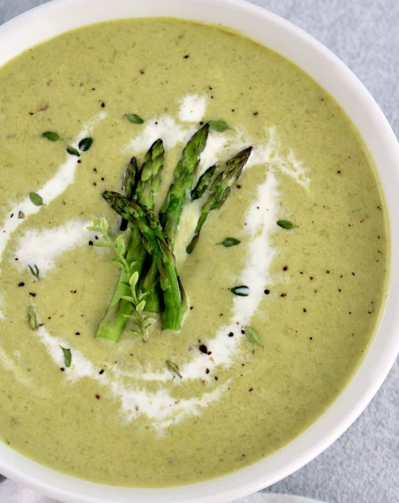 Cream of Asparagus Soup in white bowl with splash of heavy cream and asparagus tips on top