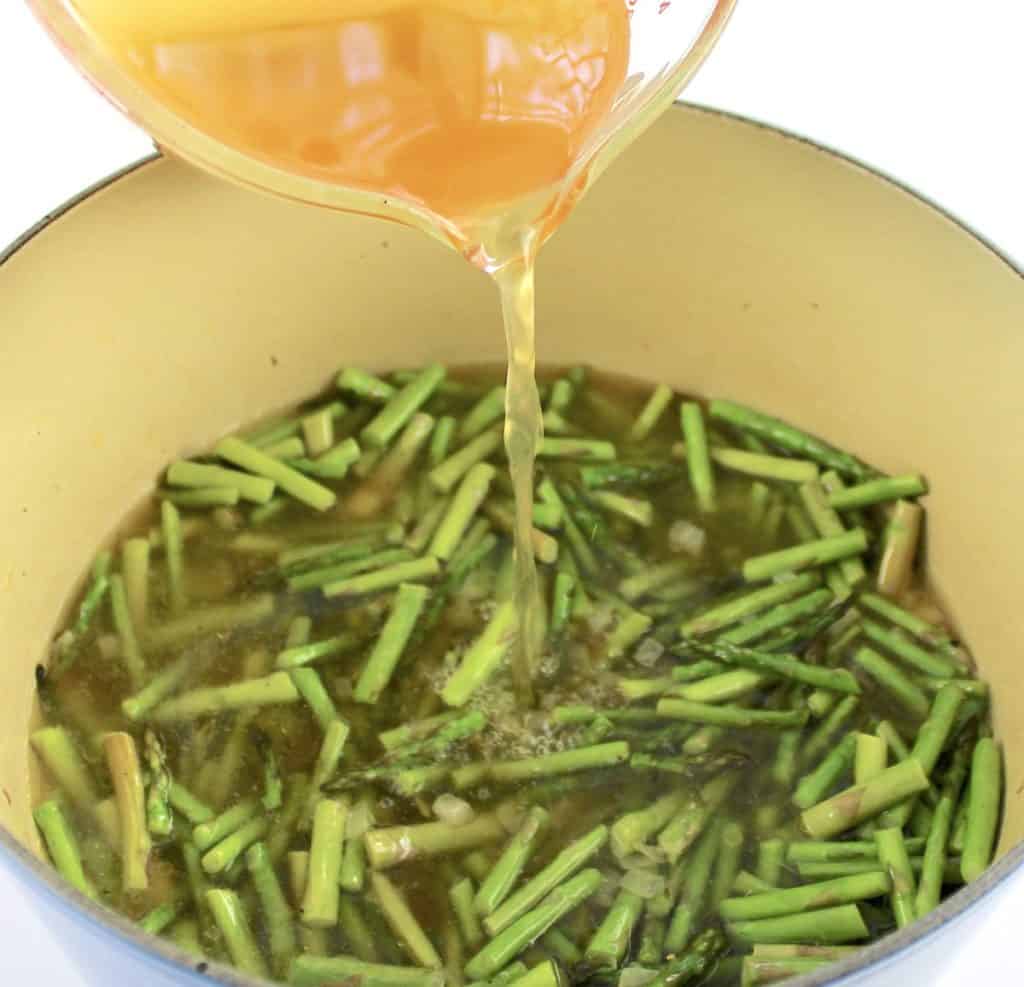 broth being poured into pot with chopped asparagus