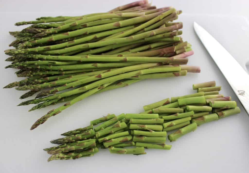 fresh asparagus on white cutting board with some chopped