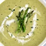 Cream of Asparagus Soup in white bowl with splash of heavy cream and asparagus tips on top