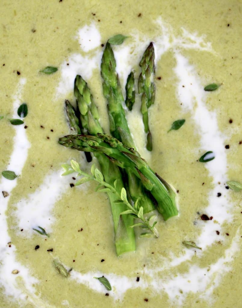 closeup of Cream of Asparagus Soup with asparagus spears on top and splash of cream