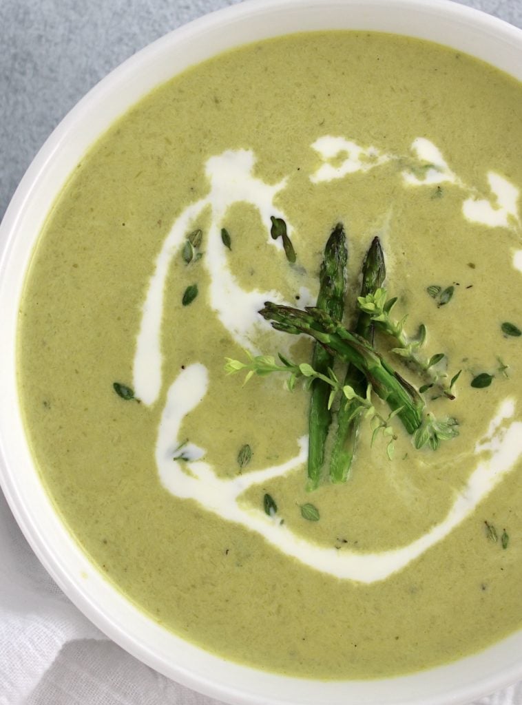 Cream of Asparagus Soup in white bowl with splash of heavy cream and asparagus tips on top