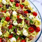 bow tie pasta salad with tomatoes mozzarella artichoke hearts and salad in glass bowl