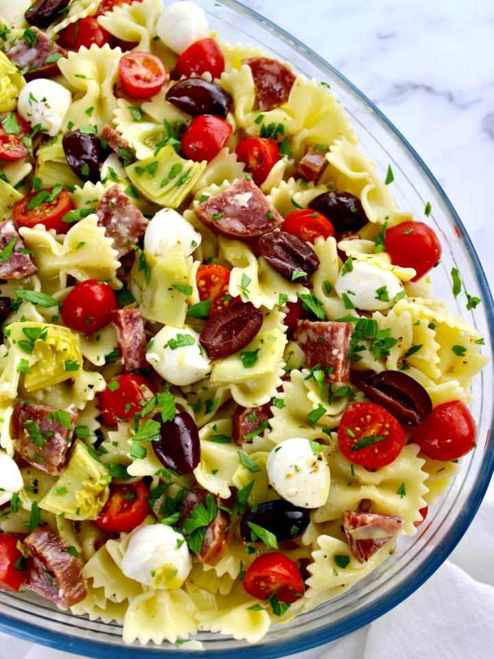 bow tie pasta salad with tomatoes mozzarella artichoke hearts and salad in glass bowl