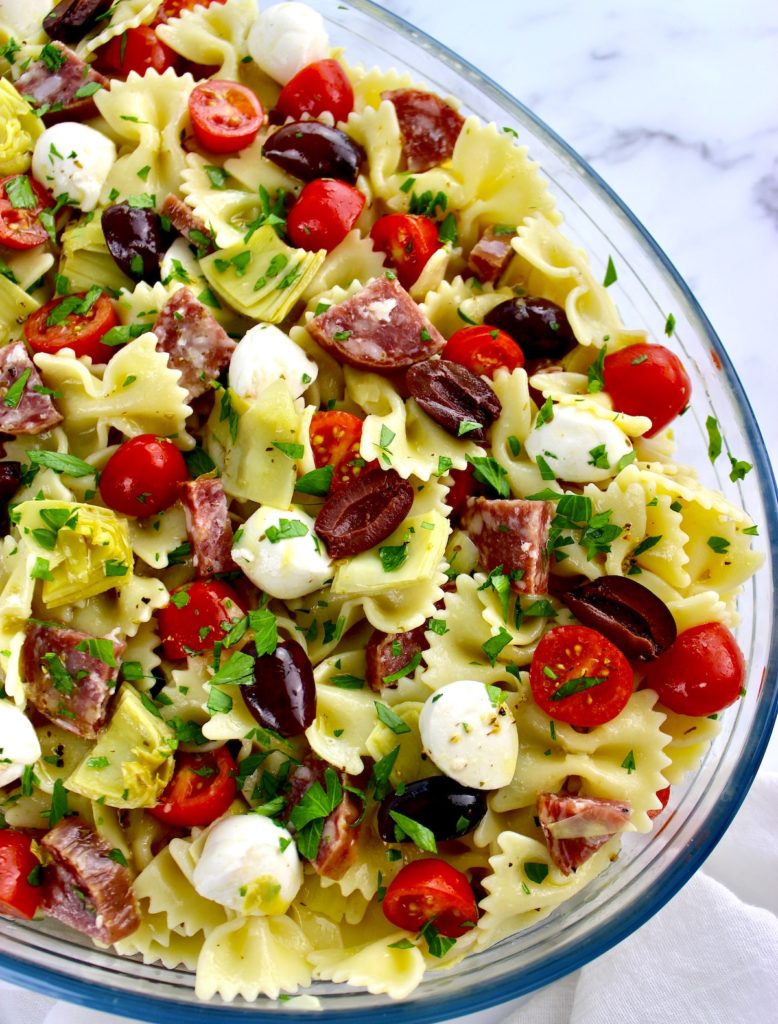 bow tie pasta salad with tomatoes mozzarella artichoke hearts and salad in glass bowl