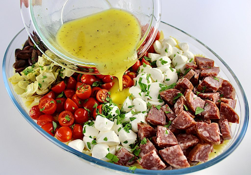 dressing being poured over pasta salad in oval glass bowl