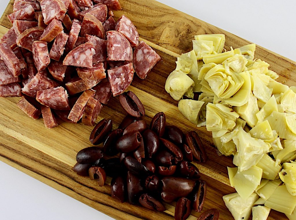 chopped salami artichoke hearts and olives on cutting board