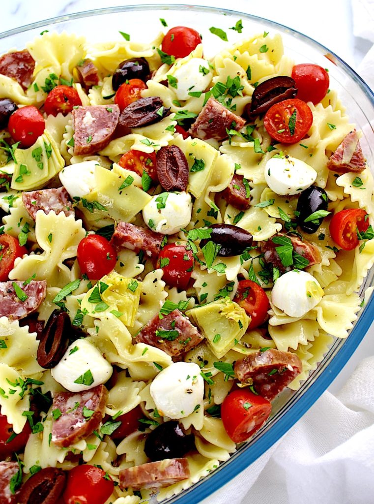bow tie pasta salad with tomatoes mozzarella artichoke hearts and salad in glass bowl