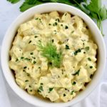Egg Salad in white bowl with chopped parsley and dill sprig on top