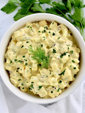 Egg Salad in white bowl with chopped parsley and dill sprig on top