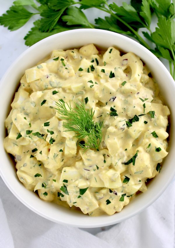 Egg Salad in white bowl with chopped parsley and dill sprig on top