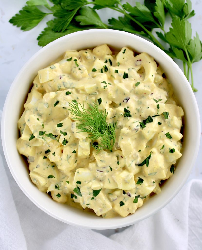 Egg Salad in white bowl with chopped parsley and dill sprig on top