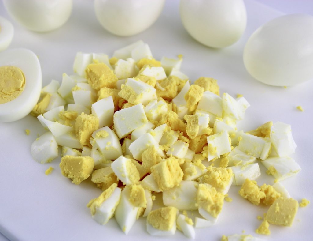 chopped hard boiled eggs on white cutting board with whole eggs in background